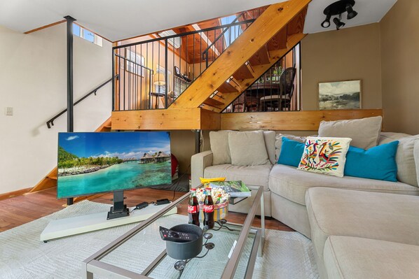 A living room with a sofa, a coffee table, a TV, and a staircase.
