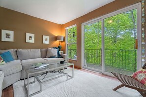 Un salon avec un canapé, une table basse et une vue sur un balcon agrémenté de plantes.