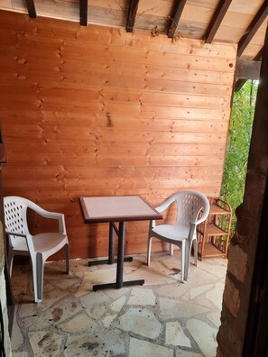 Een houten interieur met een stenen vloer, twee witte plastic stoelen en een tafel.