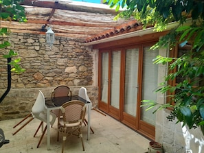 A stone wall, a tiled roof, a glass door, and a table with chairs in a courtyard.