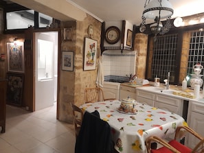 Een keuken met een eettafel, stoelen, een klok en diverse keukenbenodigdheden.