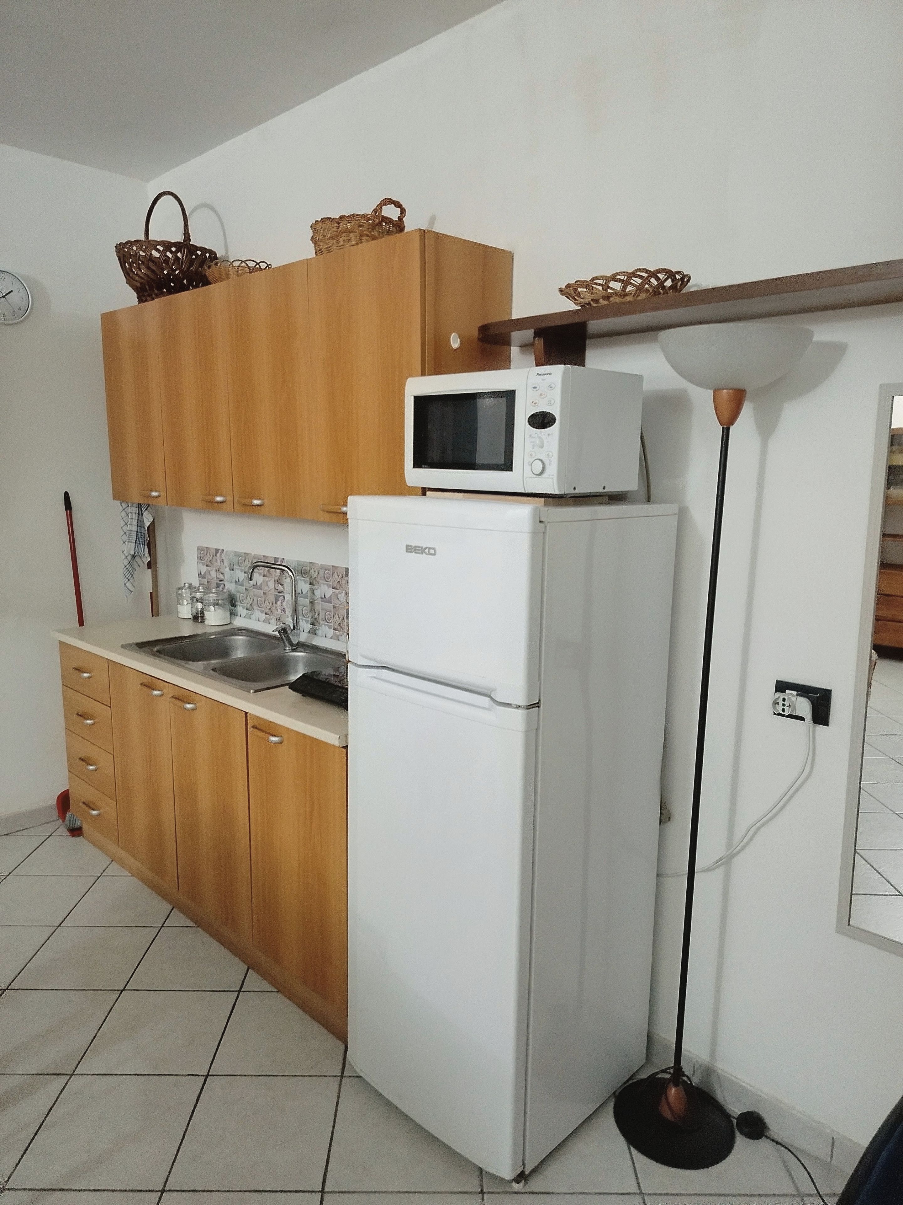 A kitchen with wooden cabinets, a white refrigerator, a microwave, and a floor lamp.