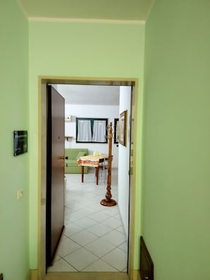 A hallway leading to a dining area with a table and chairs, a green sofa, and a framed picture on the wall. - De Blasi Studio Apartment (Lecce)