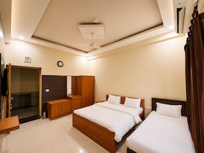 A hotel room with two beds, a wardrobe, a mirror, a clock, and a ceiling fan.
