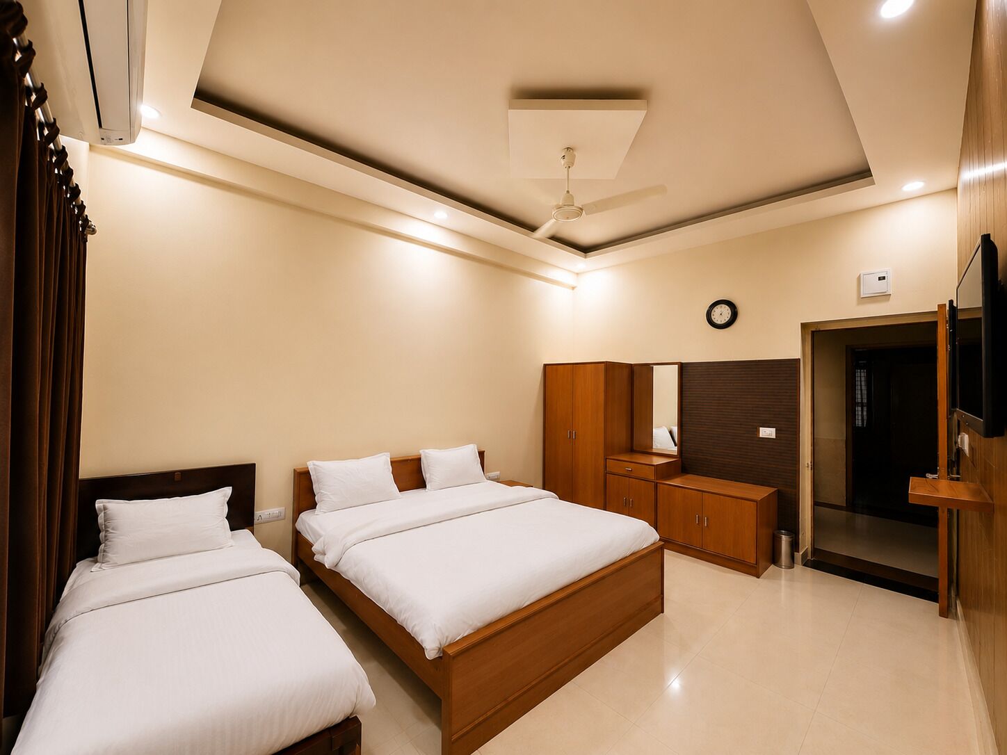 Habitación de hotel con dos camas, un armario, un espejo, un ventilador de techo y un reloj en la pared.