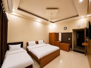 A hotel room with two beds, a wardrobe, a mirror, a ceiling fan, and a clock on the wall.