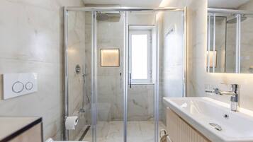 Un baño moderno con ducha envuelta en vidrio, un lavabo blanco con accesorios de cromo y un espejo sobre el lavabo.