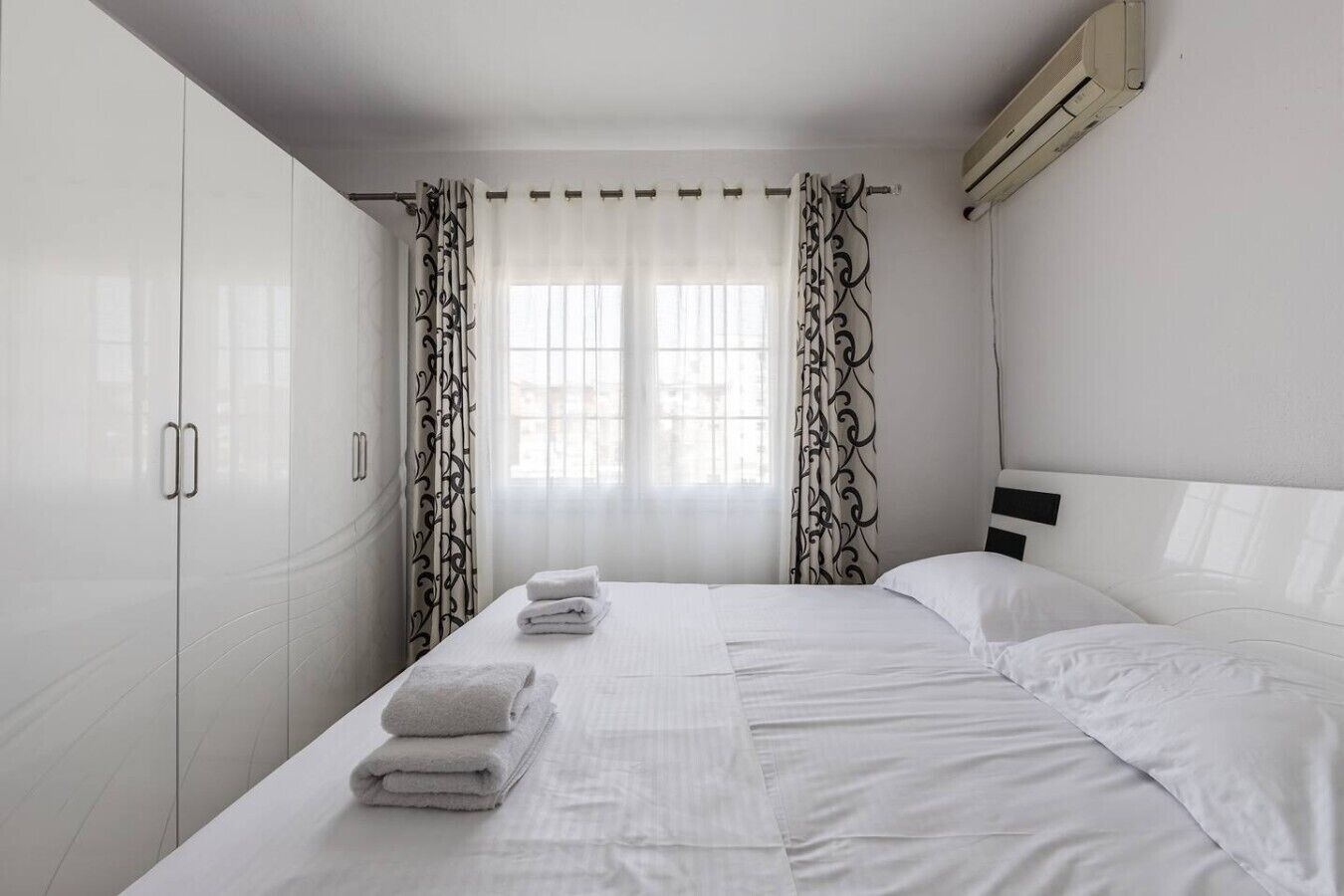 Une chambre d’hôtel avec un lit, des rideaux blancs et un appareil de climatisation.