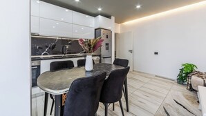A modern kitchen with white cabinets, a marble countertop, and a dining area with a marble table and black chairs. - Shkodra Living | Modern 1BR Near City Center by PikHost (Shkodër)