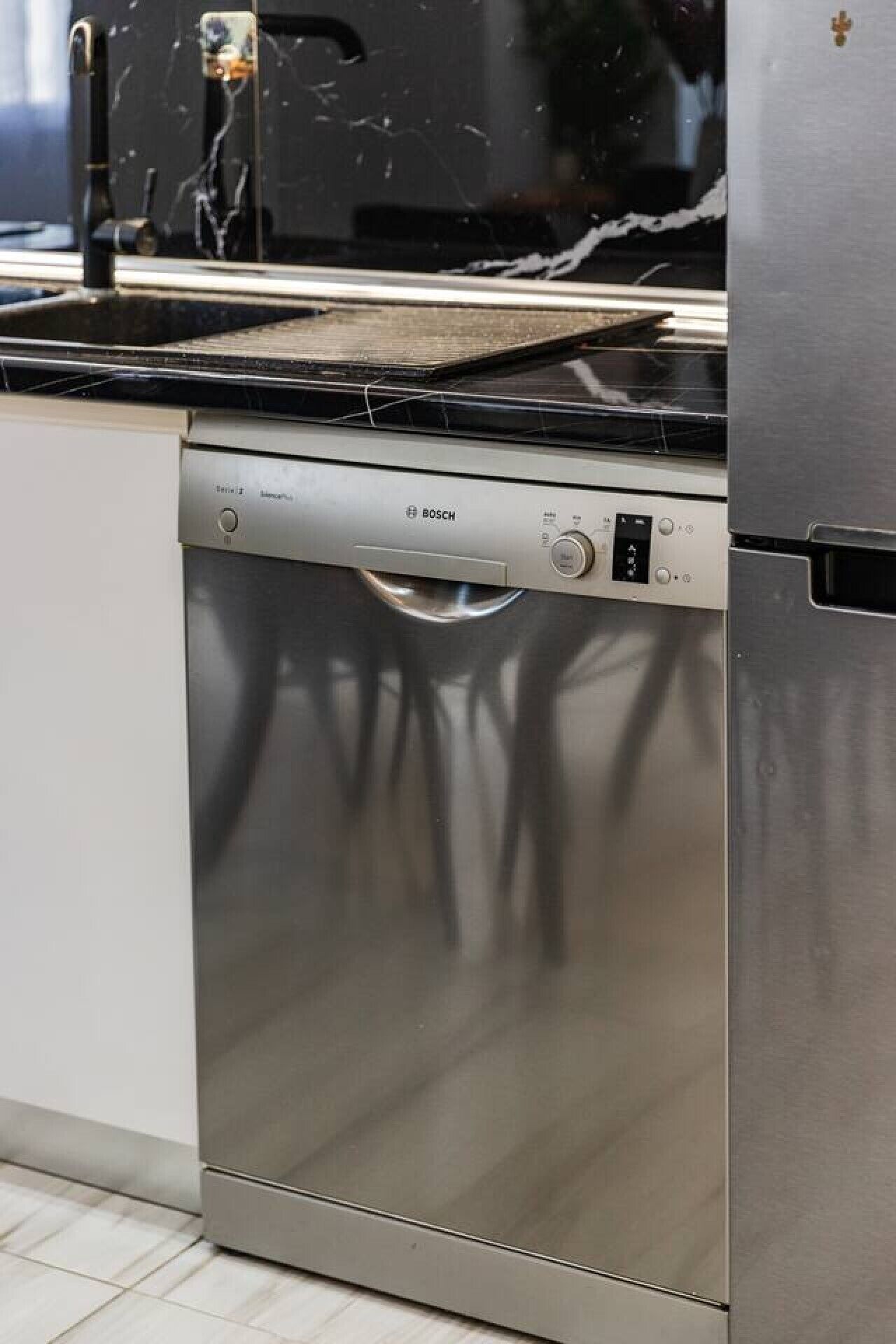 A stainless steel Bosch dishwasher in a kitchen with a black countertop and a stainless steel refrigerator.