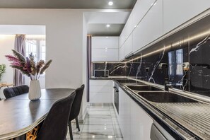 Eine moderne Küche mit schwarzem Marmorarbeitsplatz, weißen Schränken und einem Essbereich mit dunklem Tisch und Stühlen.