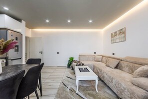 Un saló modern amb un sofà, una taula de centre, una taula de menjador amb cadires, i una zona de cuina amb un frigorífic.