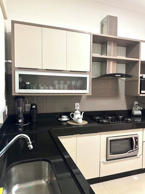 A modern kitchen with a black countertop, stainless steel sink, white cabinets, a built-in microwave, and a gas stove. - Davisis Luxo Piscina Prox Graciosa (Palmas)