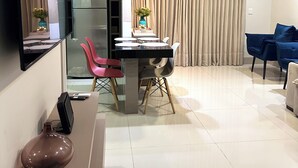 A modern living room with a dining area, a flat-screen TV, a refrigerator, a pendant light, and a large window with curtains. - Davisis Luxo Piscina Prox Graciosa (Palmas)