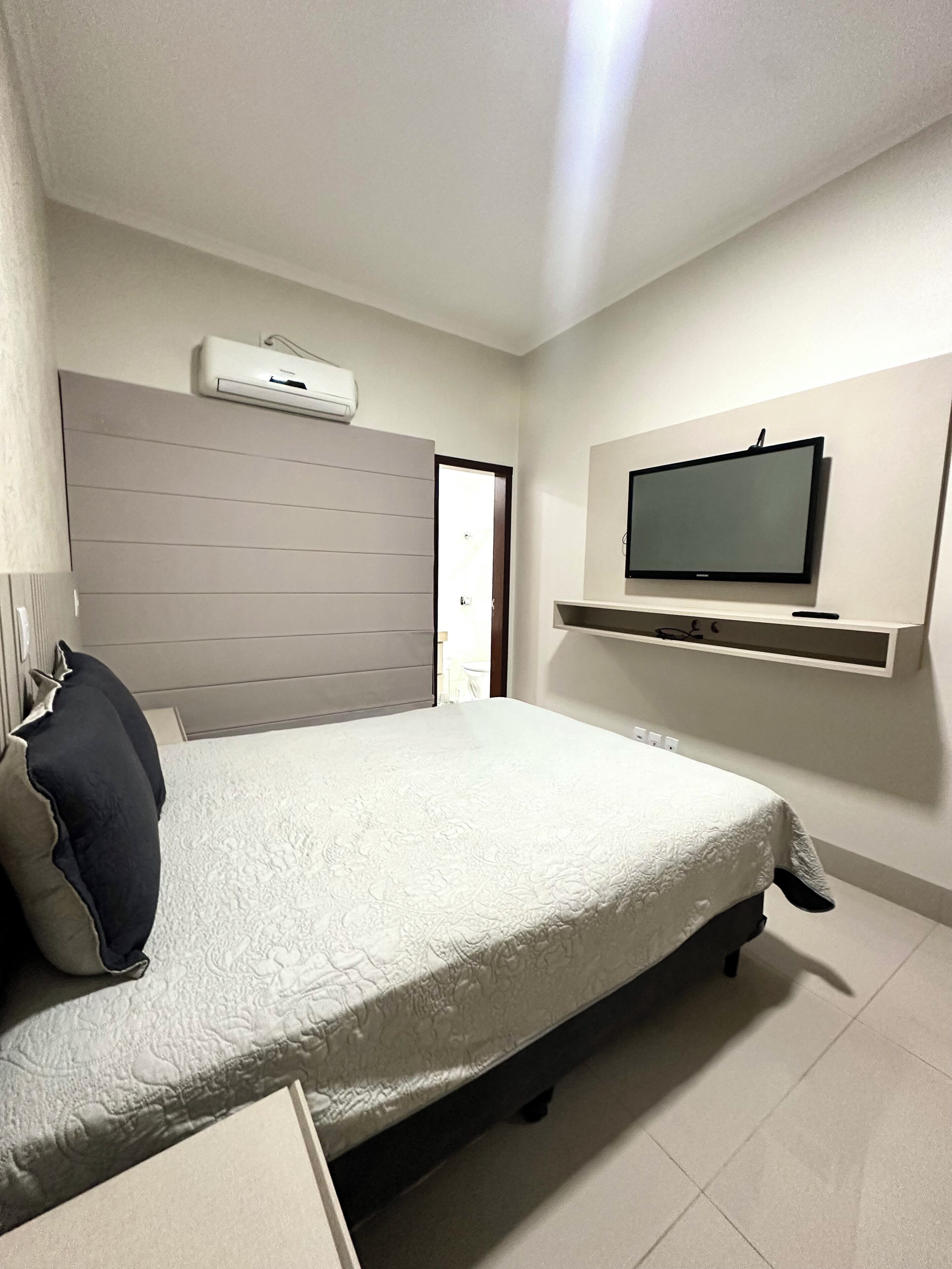 A bedroom with a bed, a television on a wall, a door, and an air conditioning unit.