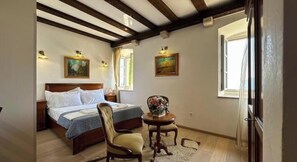 A bedroom with a bed, a chair, a small table with a vase, and two paintings on the wall. - Mistral Studio – Historic Charm, Stunning Views & Relaxing Terrace (Herceg Novi)