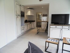 Un espacio habitable compacto con kitchenette, zona de comedor y sala de estar con televisor.