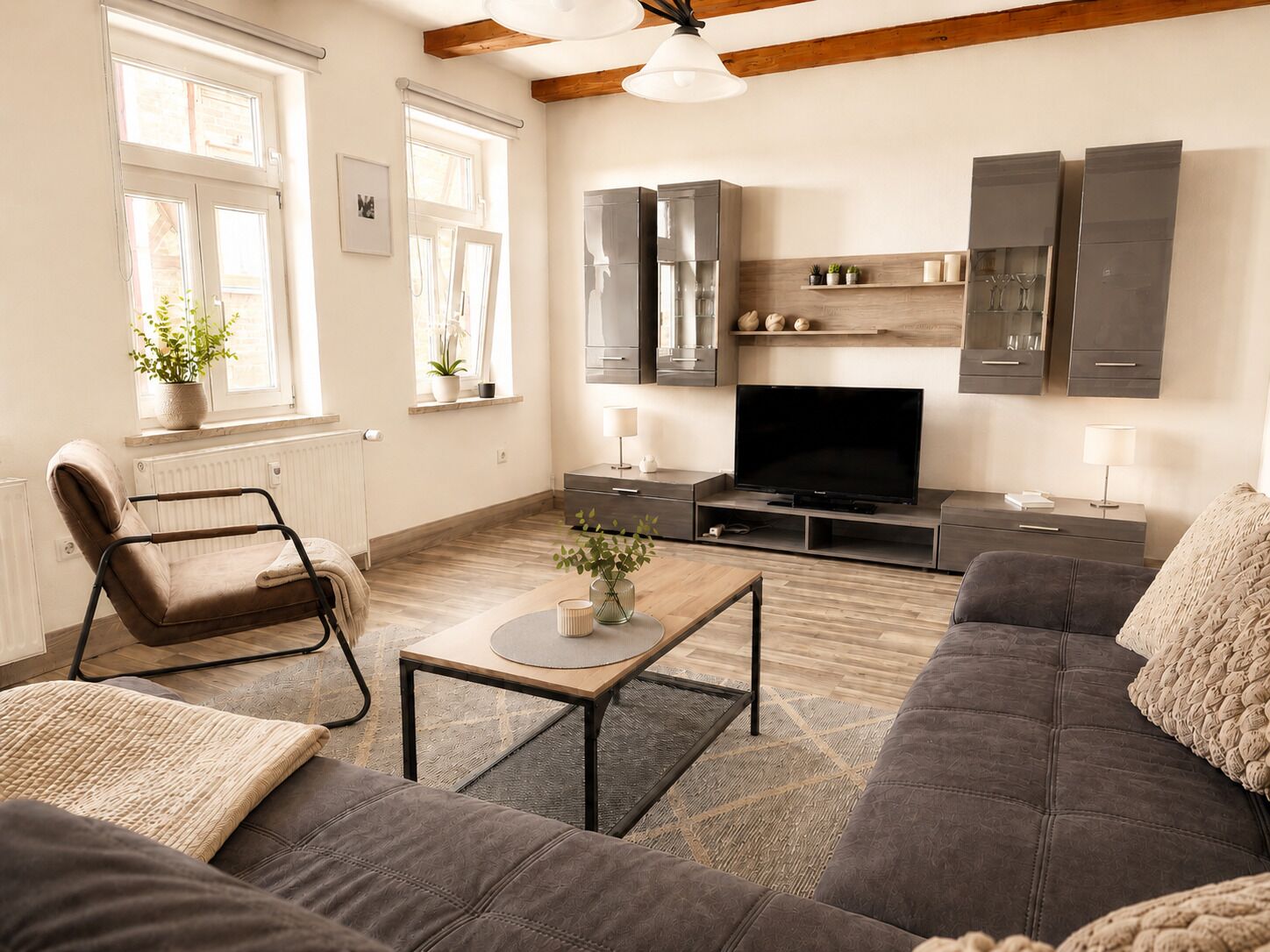 A living room with a sofa, armchair, TV, and wooden flooring.