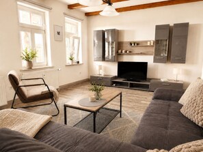 Ein Wohnzimmer mit Sofa, Sessel, Fernseher und Holzboden.