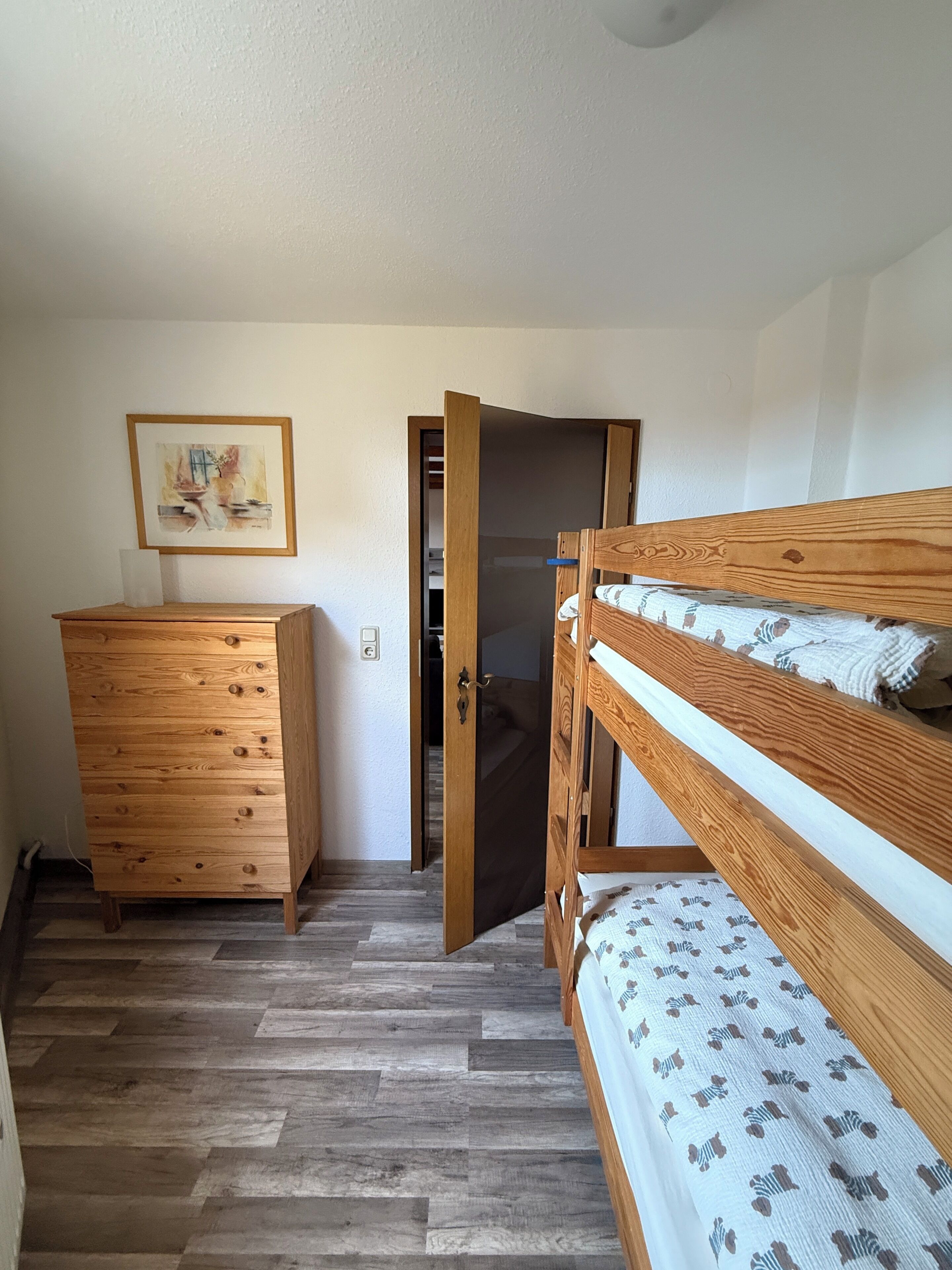 Ein Schlafzimmer mit einem Etagenbett, einem hölzernen Schminktisch und einer Tür zu einem anderen Raum.