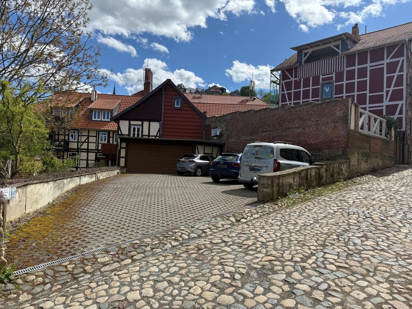 Eine Kopfsteinpflasterstraße mit parkenden Autos, traditionellen Fachwerkhäusern und einem Backsteinhaus.