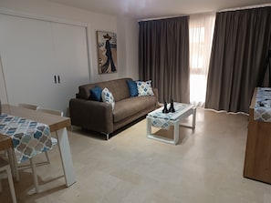 Ein Wohnzimmer mit einer Couch, einem Couchtisch, einem Esstisch und einem Gemälde an der Wand.