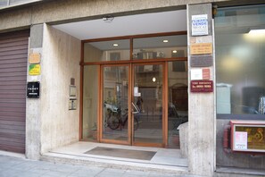Ein Gebäudeeingang mit Glastüren, ein Fahrrad davor abgestellt und mehrere Schilder an der Wand.