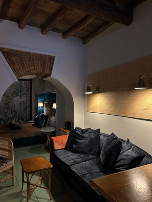 A cozy room with a dark sofa, a small wooden table, a wicker chair, and a wall-mounted lamp. - Farnese Muse (Roma)