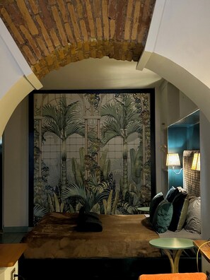 A room with a bed, a small round table, and a decorative wall with a tropical mural. - Farnese Muse (Roma)