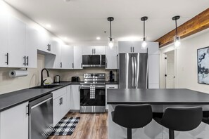 A modern kitchen with stainless steel appliances, a central island with seating, and pendant lighting. - Duckworth Suite2B Kitchen, W/D & WiFi DT (St. John's)