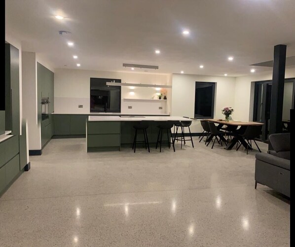 A modern kitchen with a central island, dining area with chairs, and a sofa.