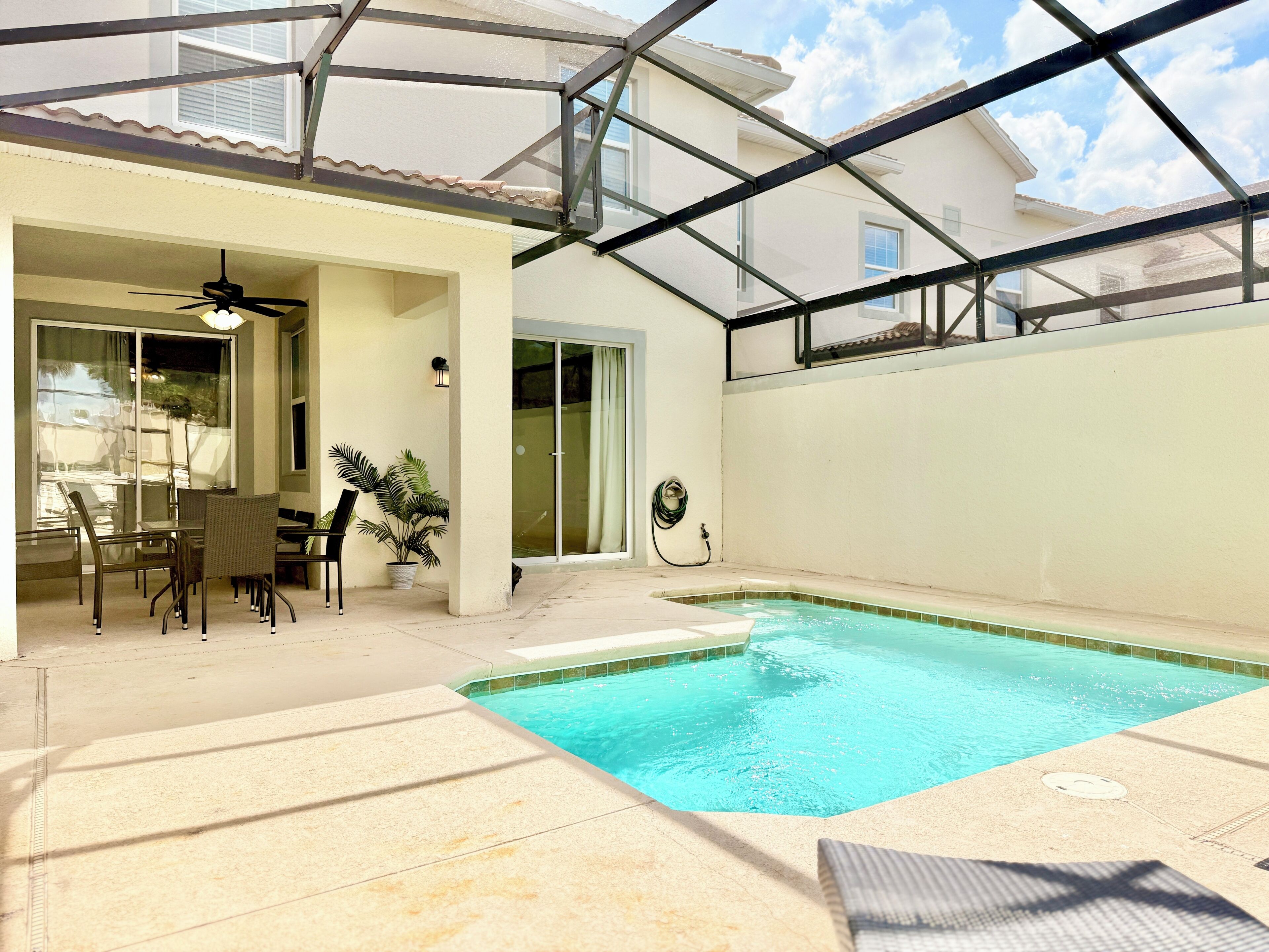 Ein Pool mit Glasveranda, eine Terrassenfläche mit Stühlen und Tisch sowie ein Deckenventilator.