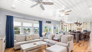 A spacious living area with a large sofa set, a coffee table, and a dining area with wooden chairs. - Waterfront Retreat w/ Private Pool & Unparalleled Views by Tybee Cottages (Tybee Island)