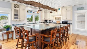 A spacious kitchen with a large island, wooden bar stools, and white cabinetry. - Waterfront Retreat w/ Private Pool & Unparalleled Views by Tybee Cottages (Tybee Island)
