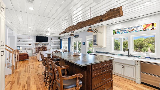 A spacious kitchen with a large island, wooden bar stools, and a rustic ceiling beam. - Waterfront Retreat w/ Private Pool & Unparalleled Views by Tybee Cottages (Tybee Island)