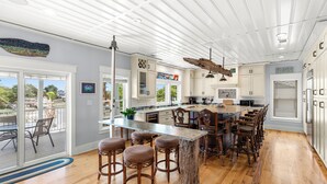 A spacious kitchen with a large island, wooden bar stools, and a view of the outdoors. - Waterfront Retreat w/ Private Pool & Unparalleled Views by Tybee Cottages (Tybee Island)