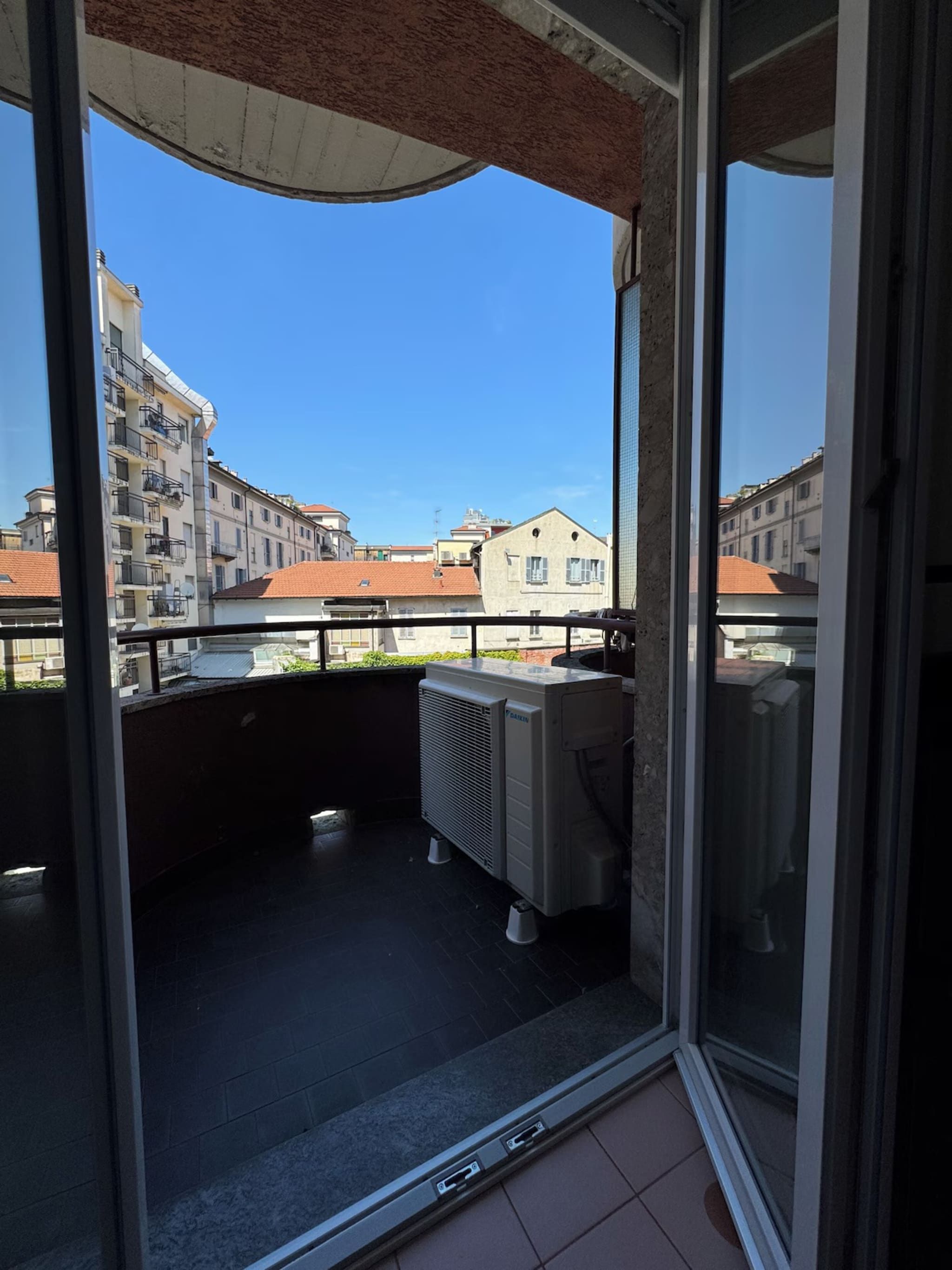 Un balcon donnant sur des immeubles et équipé d’un grand appareil de climatisation.