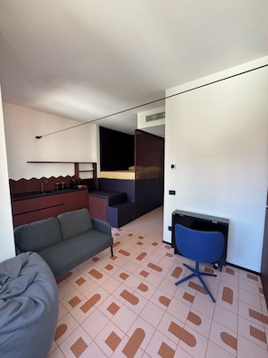 A compact room with a sofa, a desk with a chair, a bed with a canopy, and a kitchenette area. - Studio Apartment with Balcony and Parking, 206 (Milano)