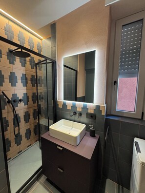 A modern bathroom with a glass-enclosed shower, a large mirror, and a vanity with a sink. - Studio Apartment with Balcony and Parking, 206 (Milano)