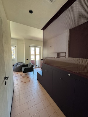 A modern interior with a dark-colored cabinet, a grey sofa, and a patterned wall. - Studio Apartment with Balcony and Parking, 206 (Milano)