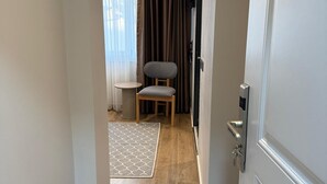 A hallway leading to a room with a wooden floor, a grey chair, a small table, and a window with curtains. - Armira Hotel Old City (İstanbul)