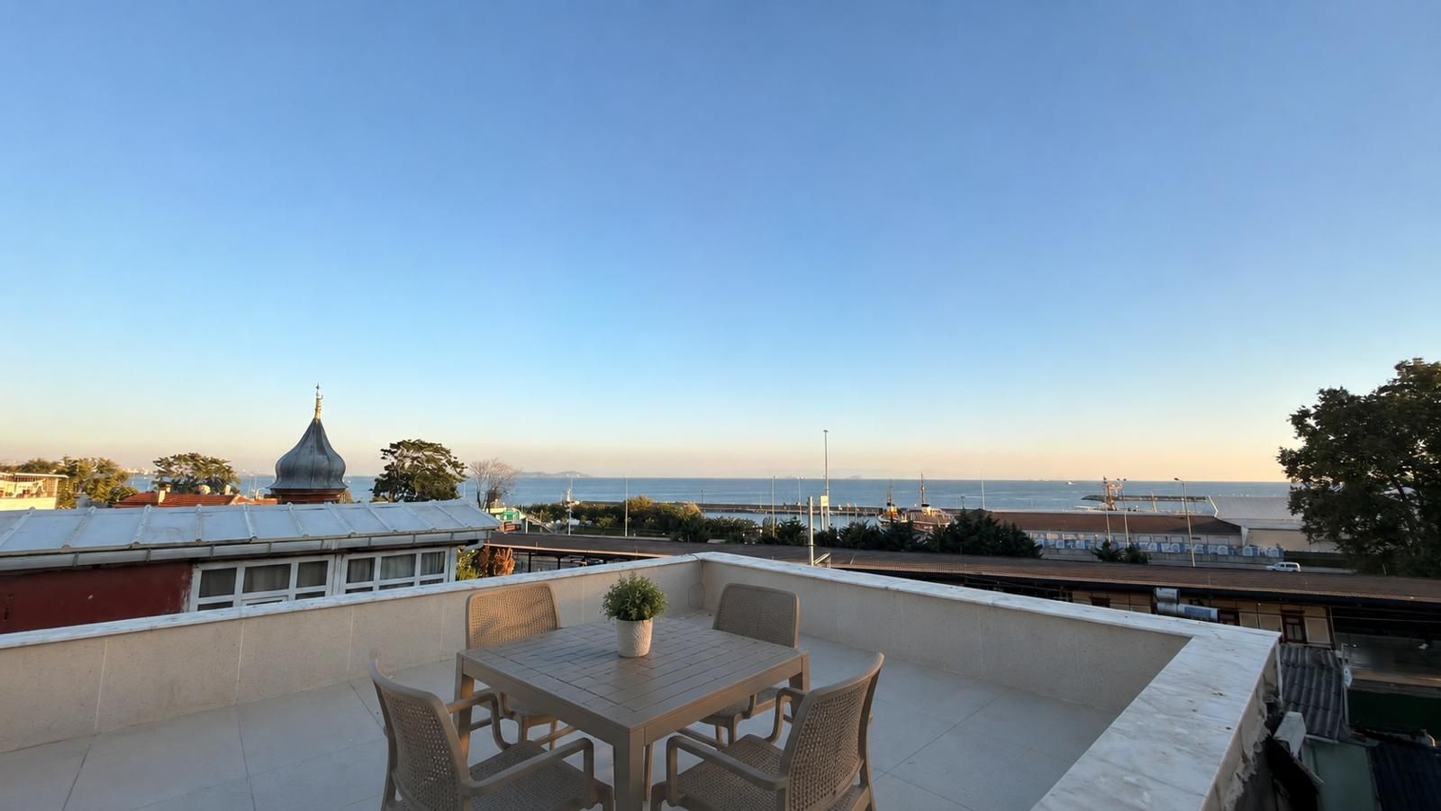 Terraço no telhado com mesa e cadeiras, com vista para a costa e o mar, incluindo uma ponte.
