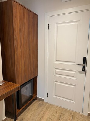 Una habitación con un armario de madera, una puerta blanca con picaporte y un televisor sobre un mueble.
