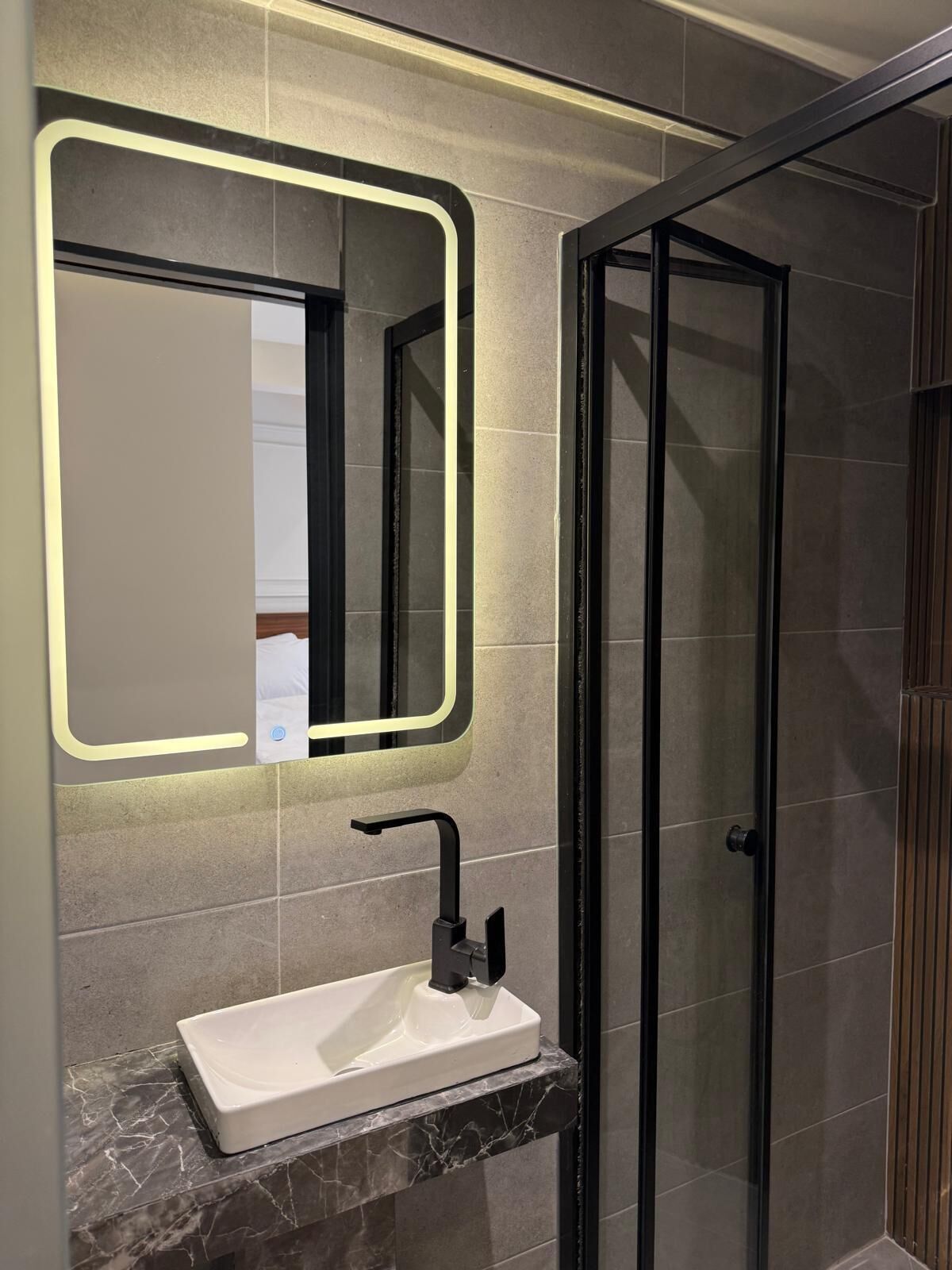 Une salle de bain avec un lavabo blanc, un miroir éclairé par une lumière néon et une cabine de douche en verre.