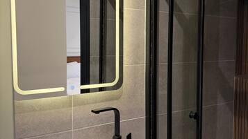Une salle de bain avec un lavabo blanc, un miroir éclairé par une lumière néon et une cabine de douche en verre.