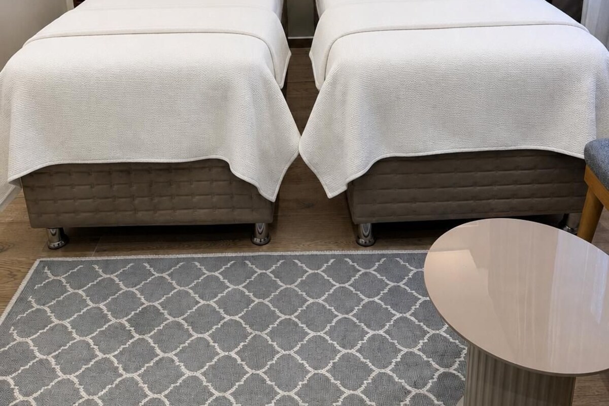 Habitación de hotel con dos camas, una mesita redonda y una alfombra estampada.