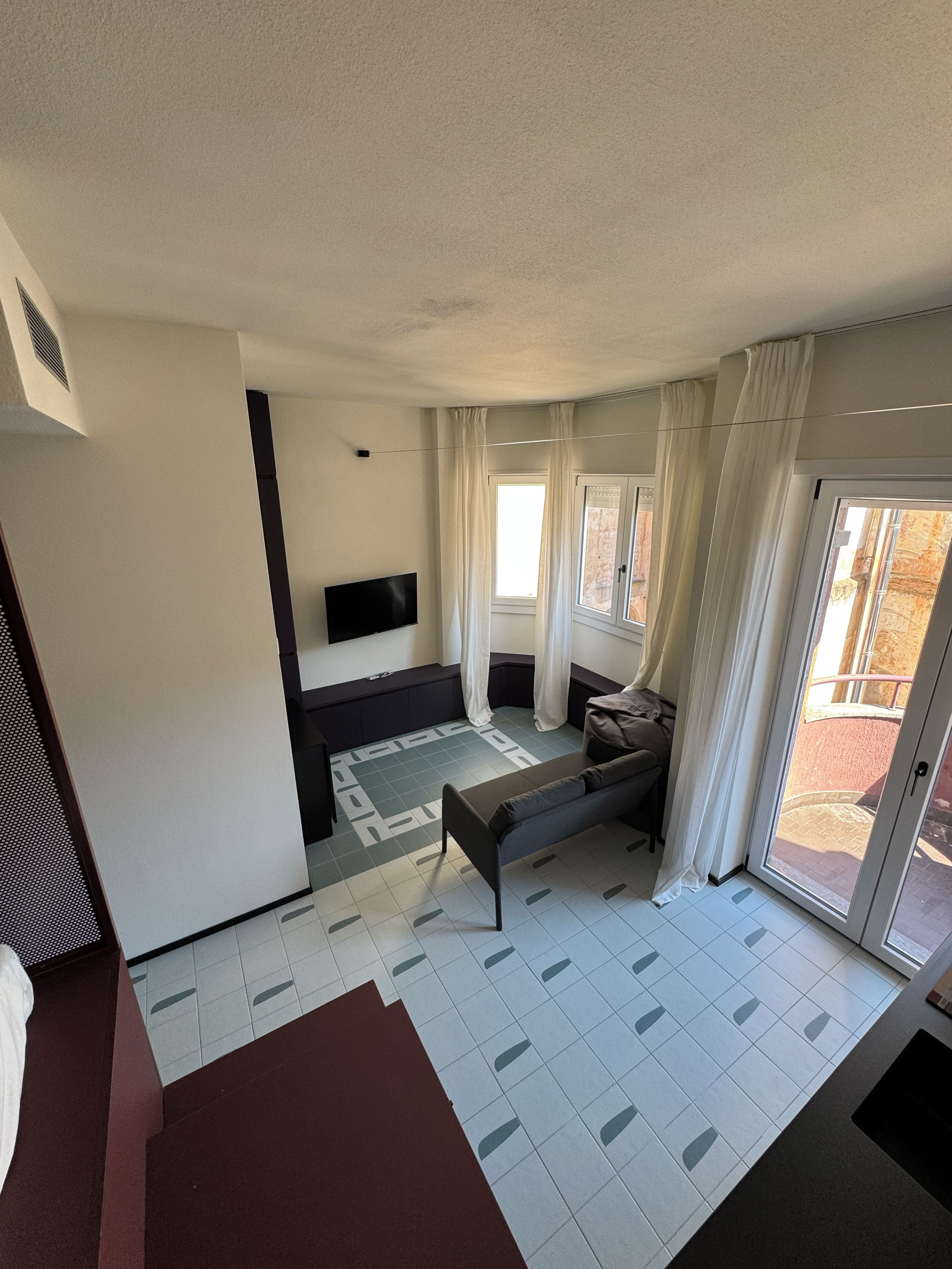A modern bedroom with a bed, a TV, and a sliding glass door to the outside.
