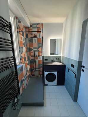 A compact bathroom with a shower, a built-in washing machine, and a sink. - Studio Apartment with Balcony and Parking, 204 (Milano)
