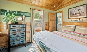 Ein Schlafzimmer mit Bett, Holzkommode und einem fenster mit Vorhängen.