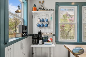 Eine Küche mit Kaffeebereich, Wasserkocher, Kaffeemaschine, Tassen und Blick auf Bäume durch das Fenster.